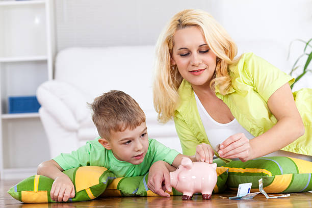 Mother and son playing with piggy bank. Little smiling boy inserting money into piggy bank.